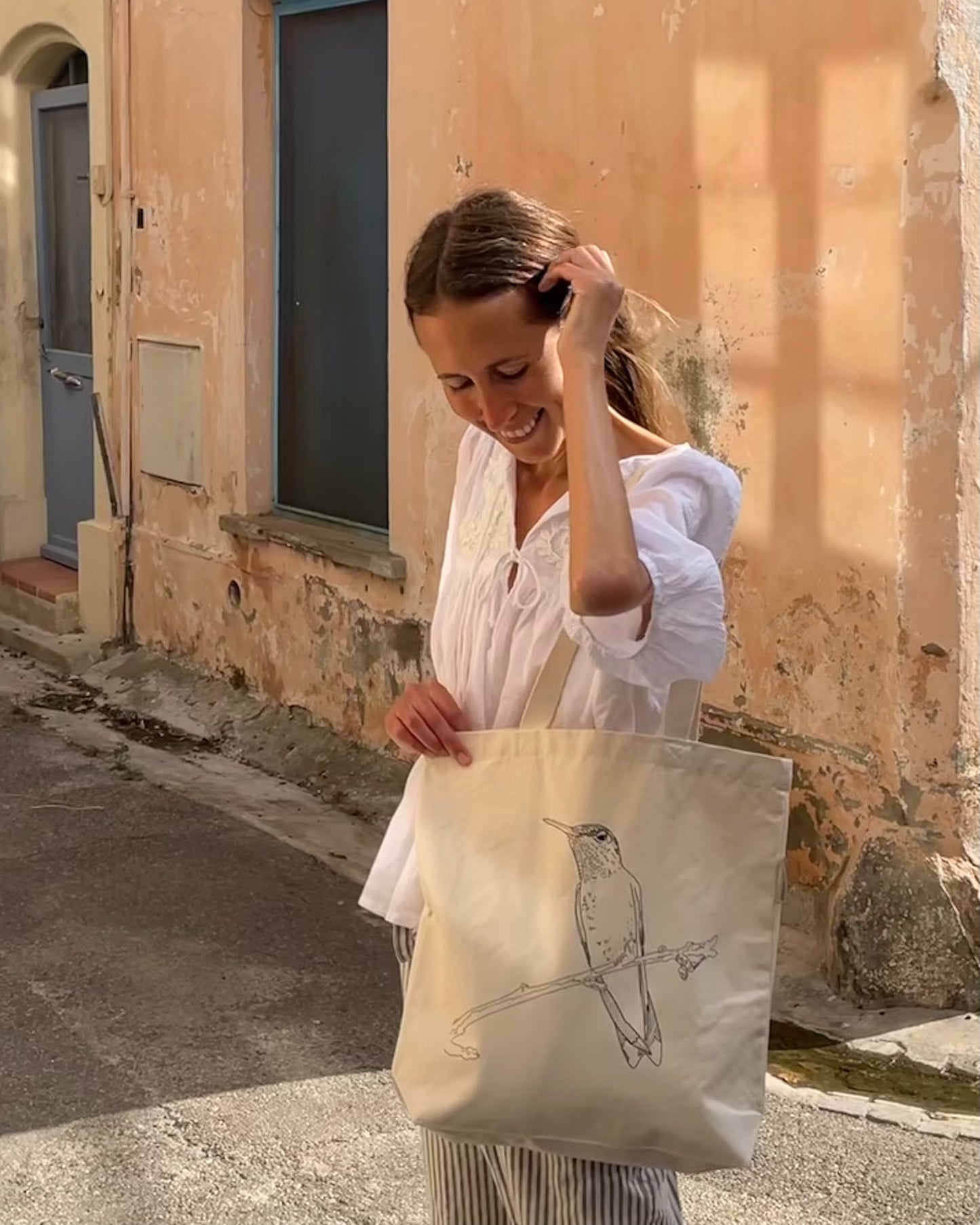 A young woman in the street carrying a tote bag with a printed drawing of a hummingbird.